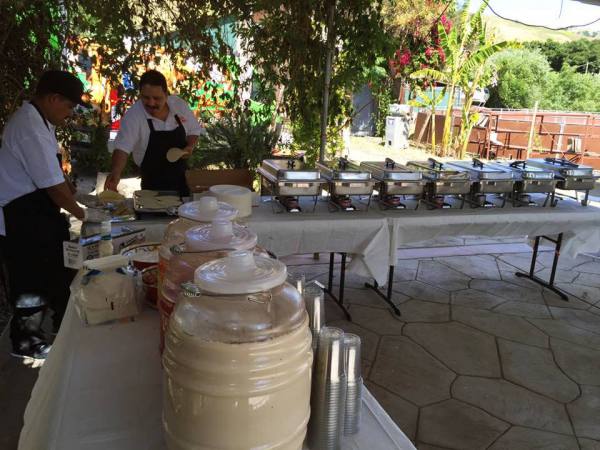 Cooks serving food at an outdoor catering table.